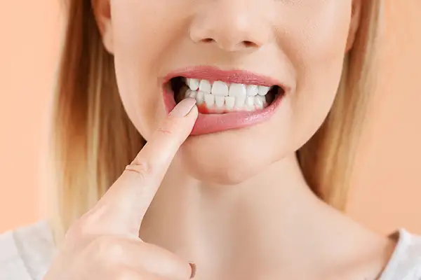 Close-up of a woman pointing at her inflamed gums, a symptom of periodontal disease, emphasizing the need for periodontal care.